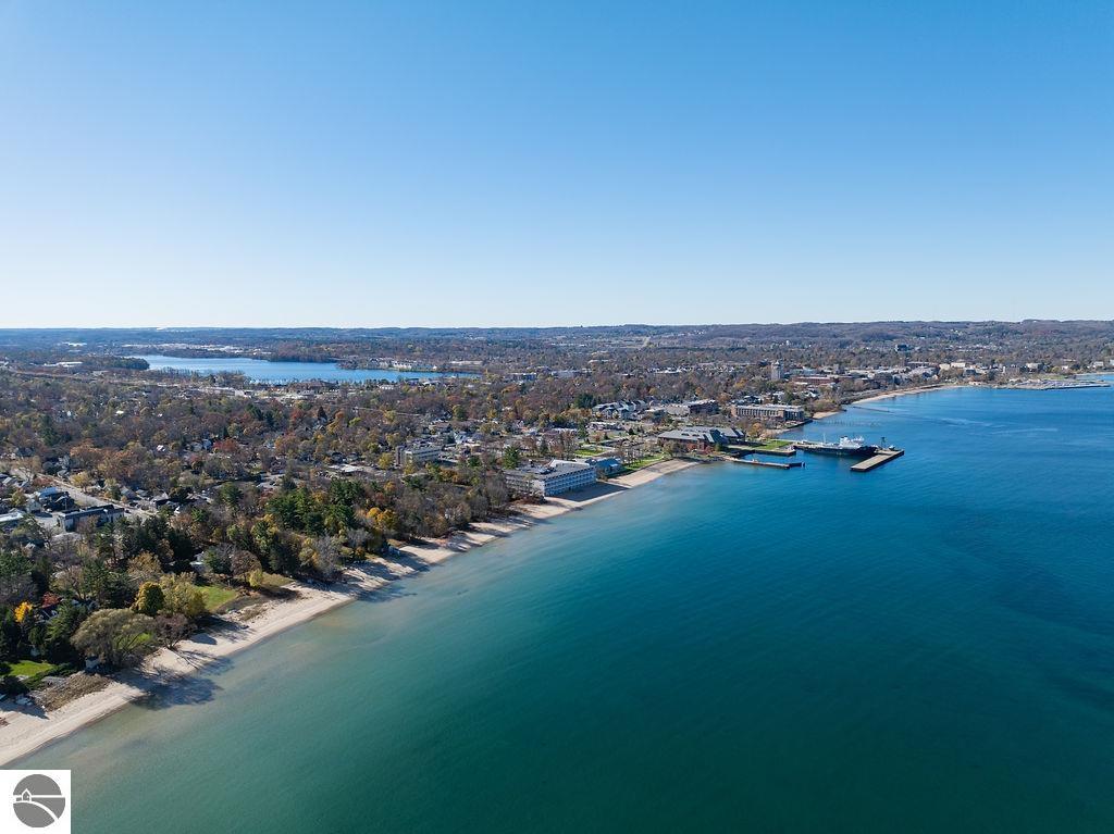 Aerial shoreline with sandy beaches, autumn-colored trees, waterfront buildings, and marina docks.