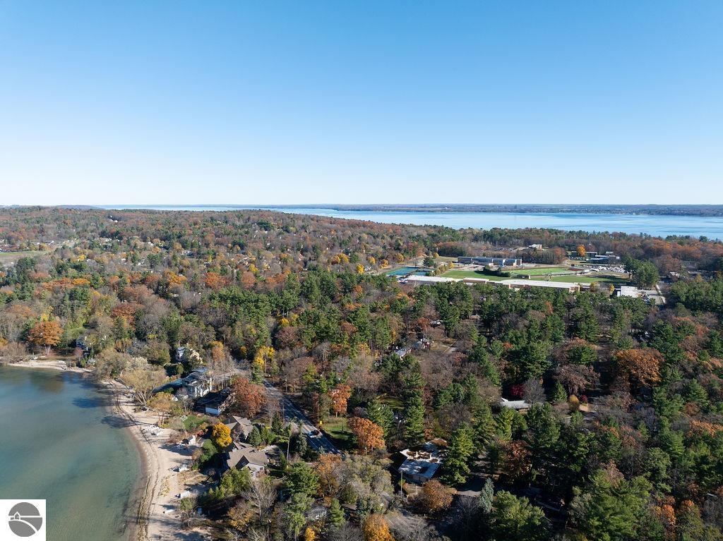 Aerial shoreline with lakeside homes, sandy beach, autumn woods, and lake views.