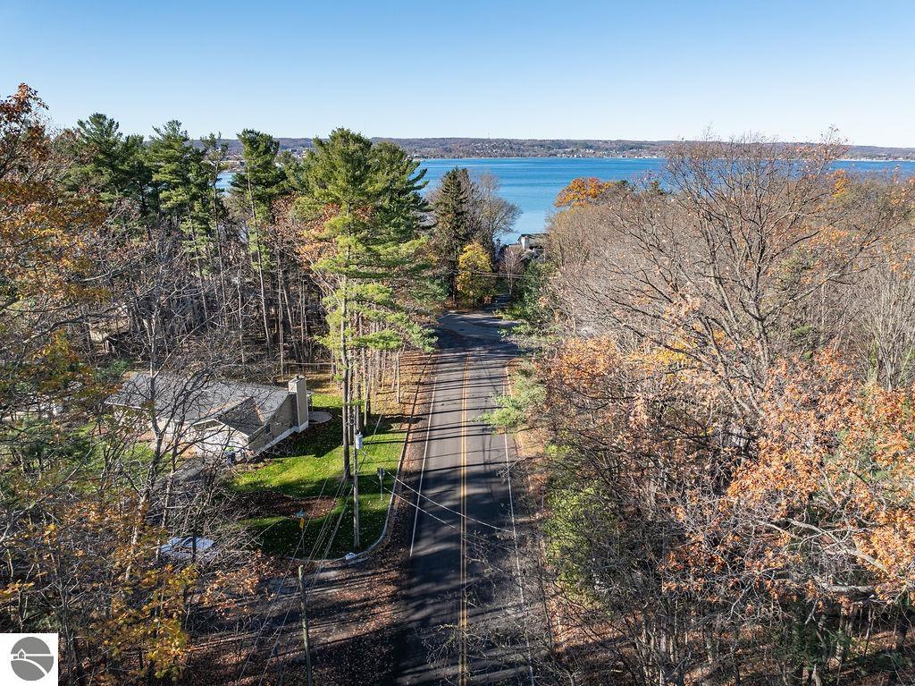 Tree-lined road leading toward blue water, with a distant shoreline and autumn foliage.