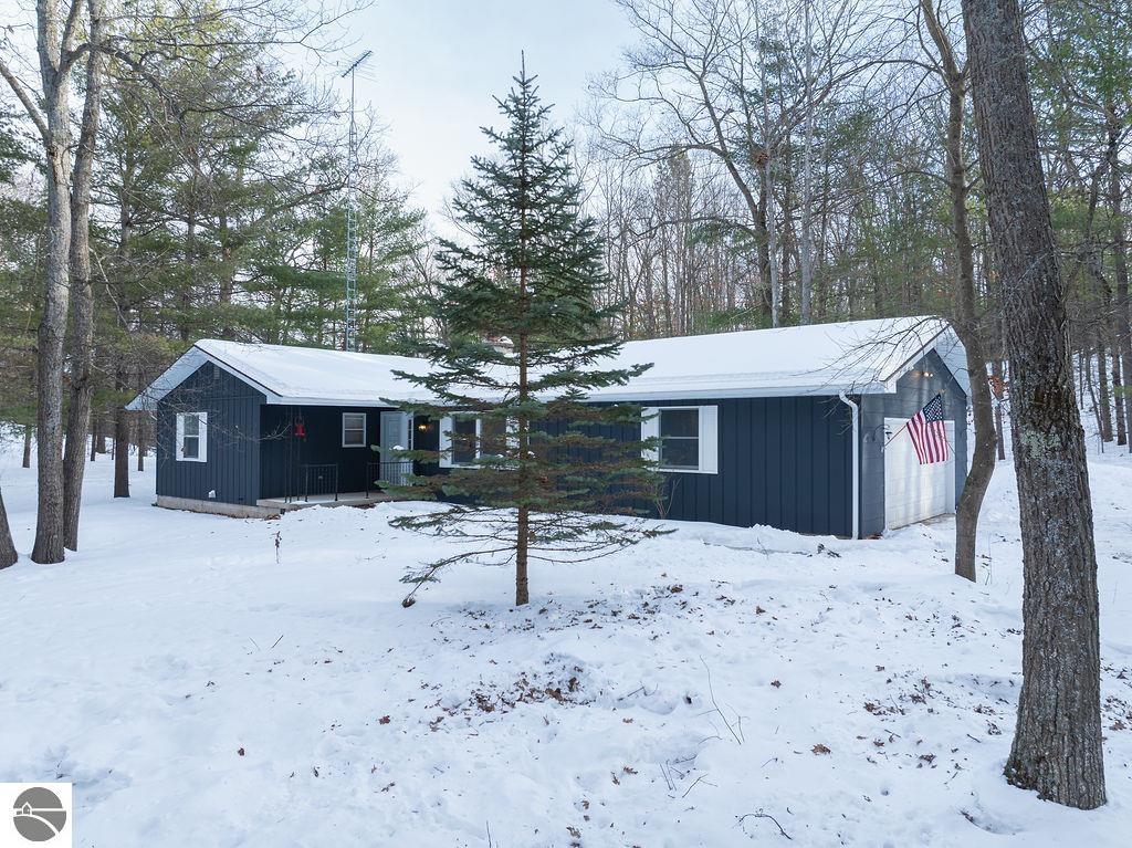 Dark blue single-story home with an attached garage, surrounded by snowy woodland.