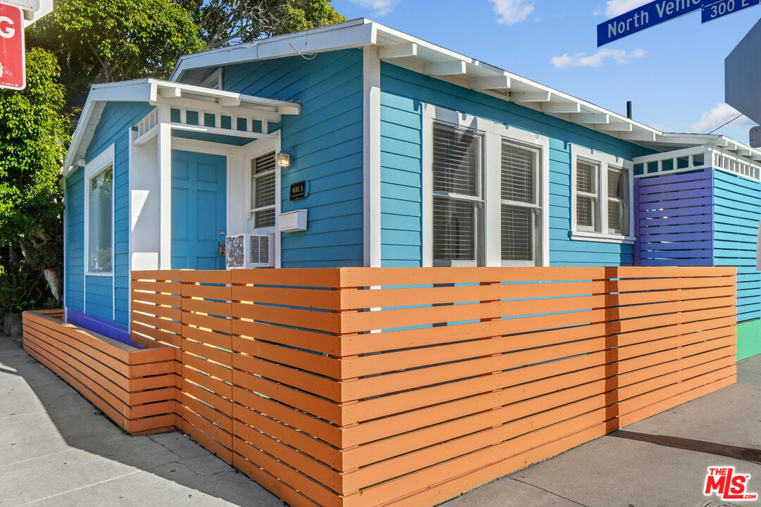 Turquoise bungalow with white trim, an orange slatted fence, and a purple side wall.