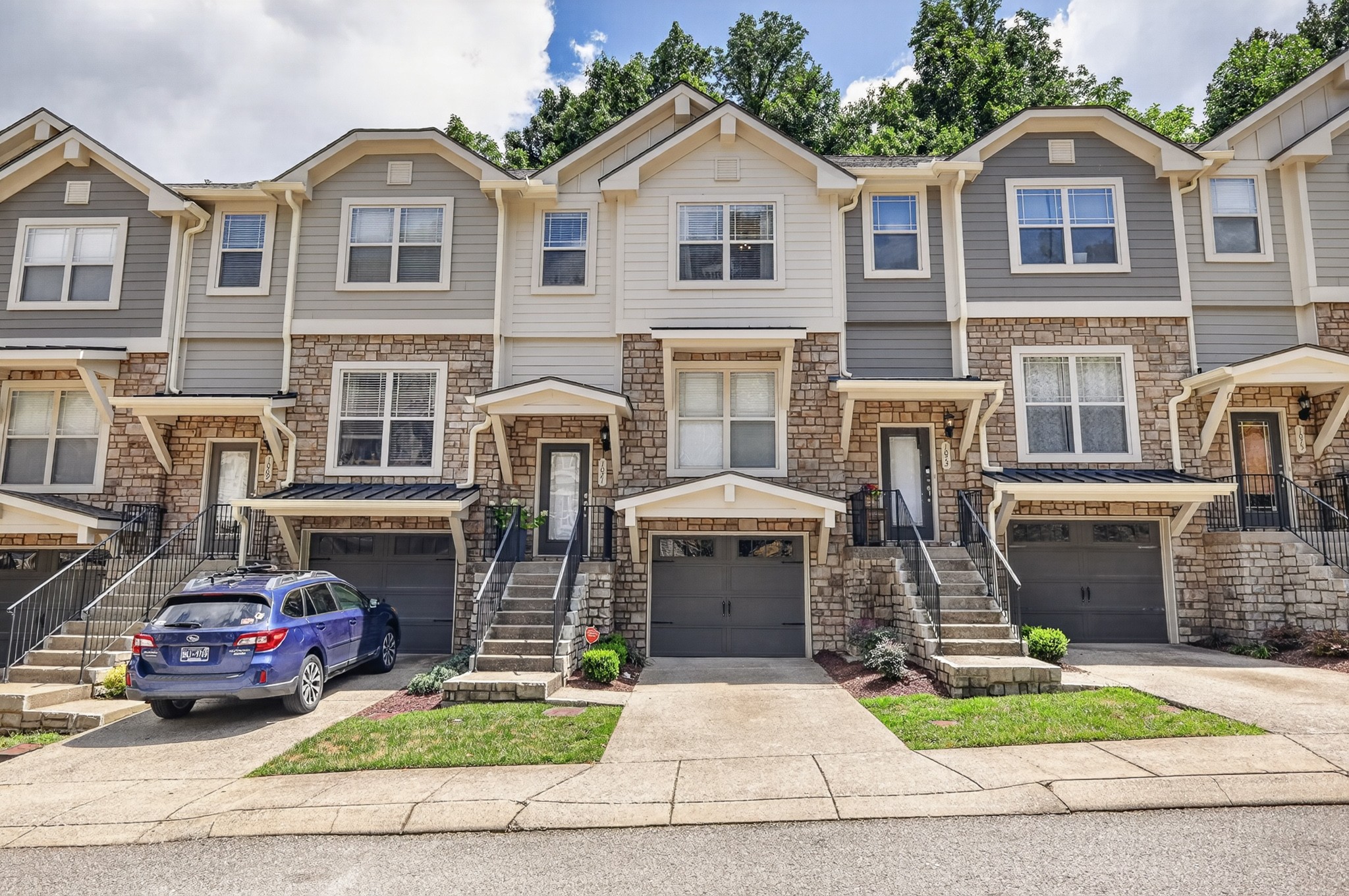 Attached gray townhome with stone facade, front stairs, and garage; a blue SUV is parked in the neighboring driveway.
