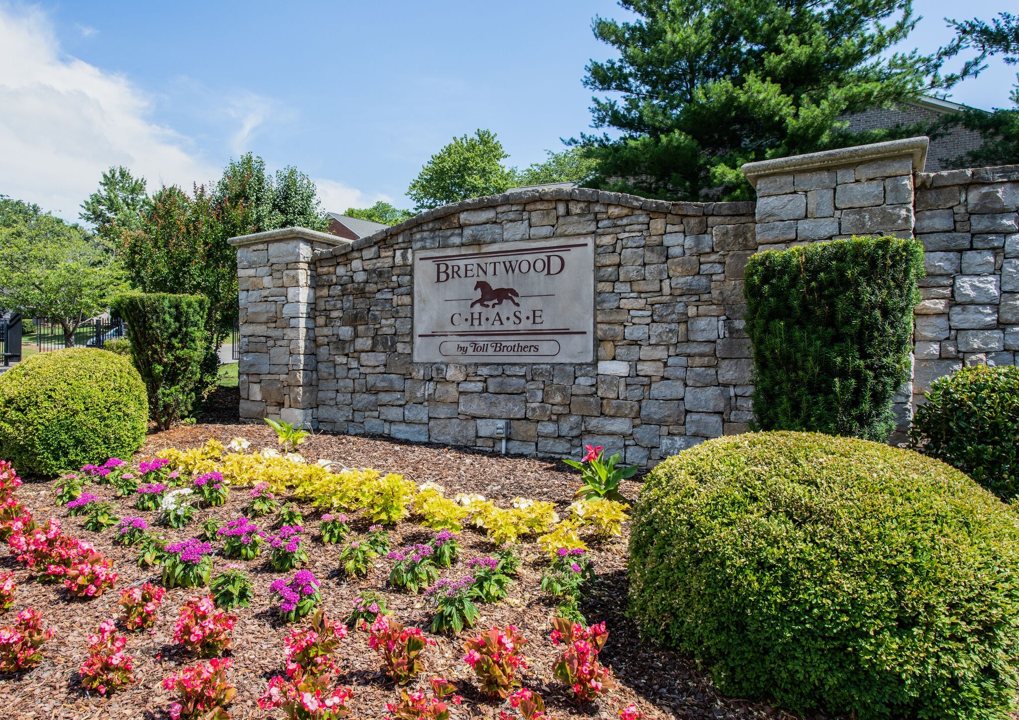 Brentwood Chase stone entrance sign amid flowering landscaping and trimmed shrubs.