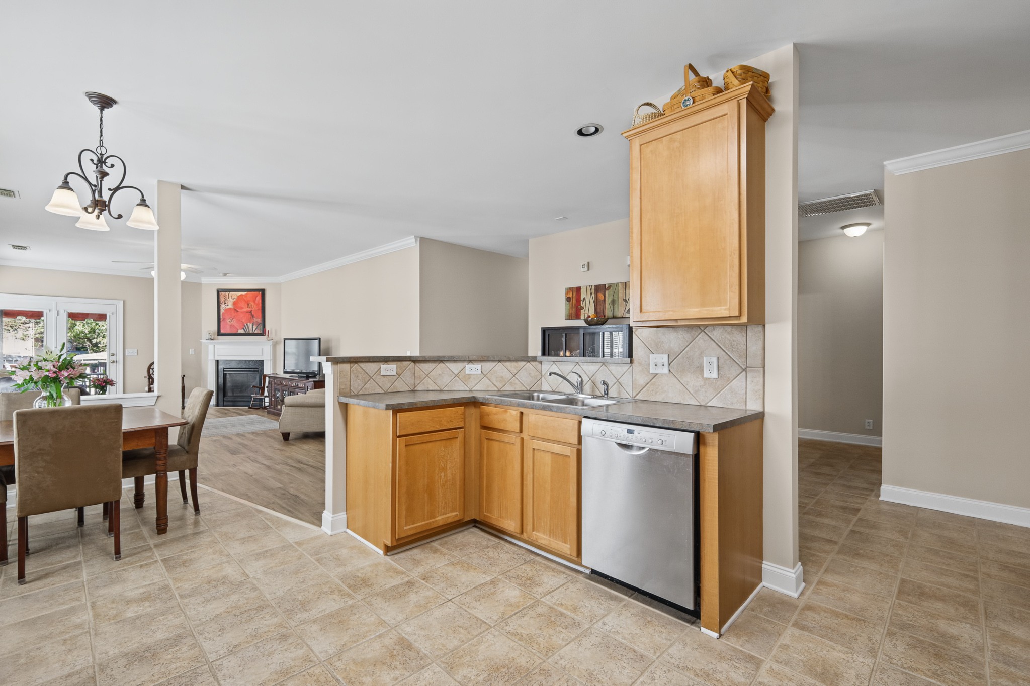 Open kitchen with wood cabinets and tiled backsplash, dining table and living room with fireplace beyond.