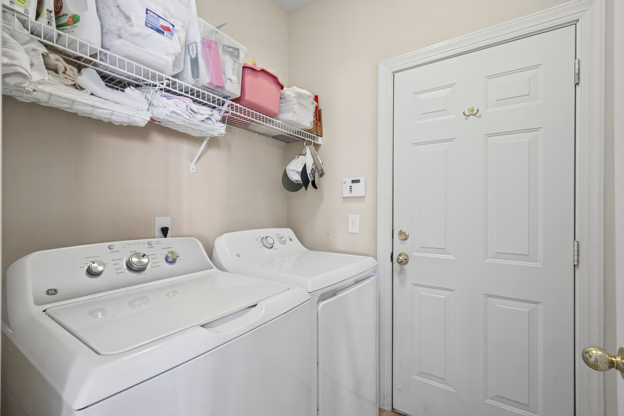 Laundry room with a white washer and dryer beneath shelves of towels and supplies.