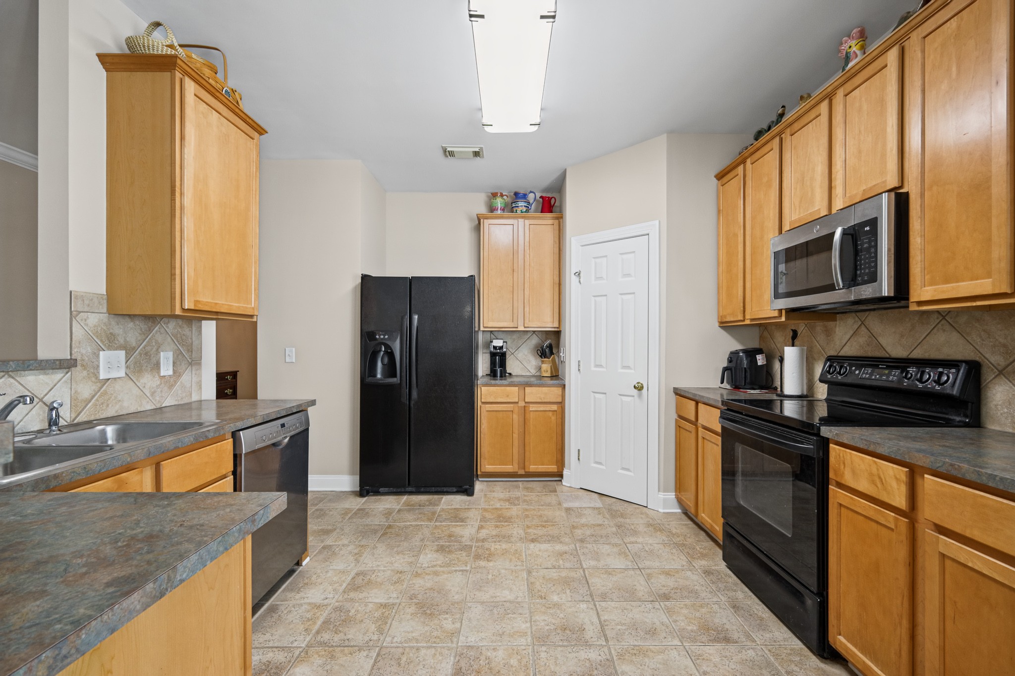 Kitchen with honey-colored cabinets, stone countertops, black appliances, and beige tile flooring.