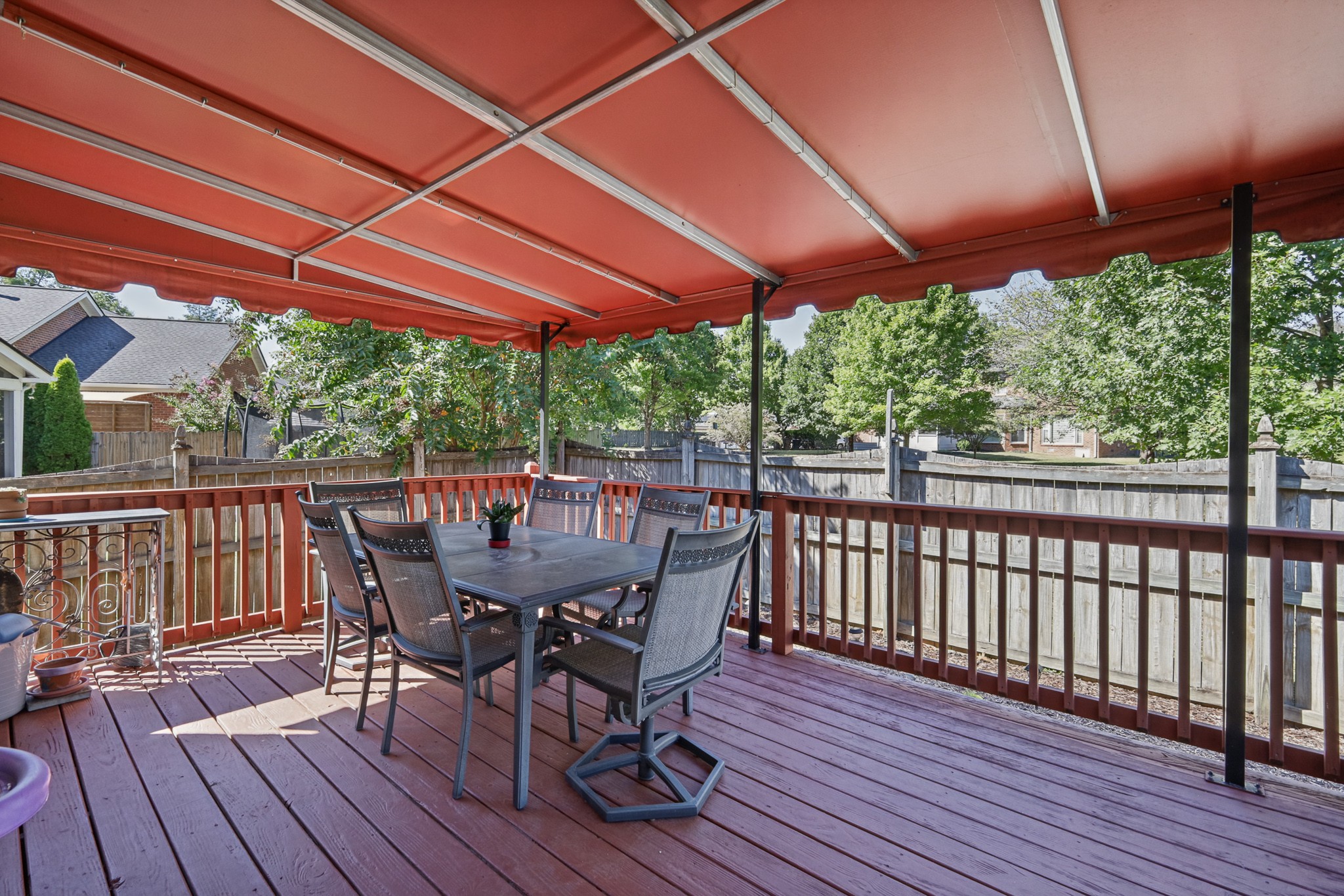 Furnished deck with a large red awning overlooking a fenced, tree-lined backyard.