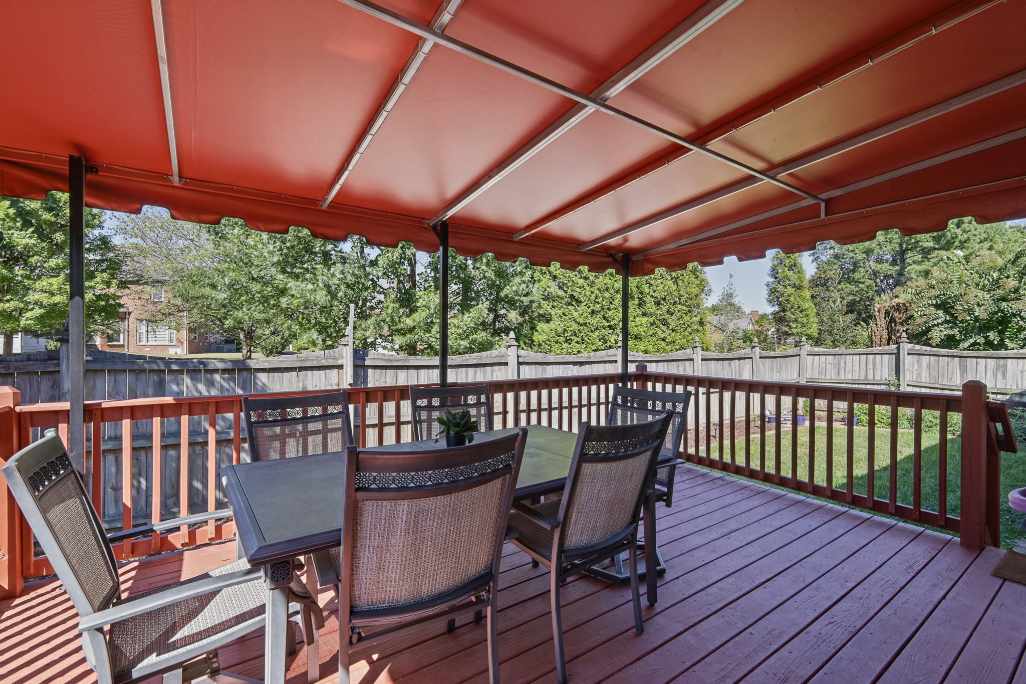 Covered wooden deck with a patio dining set and fenced, tree-lined yard.