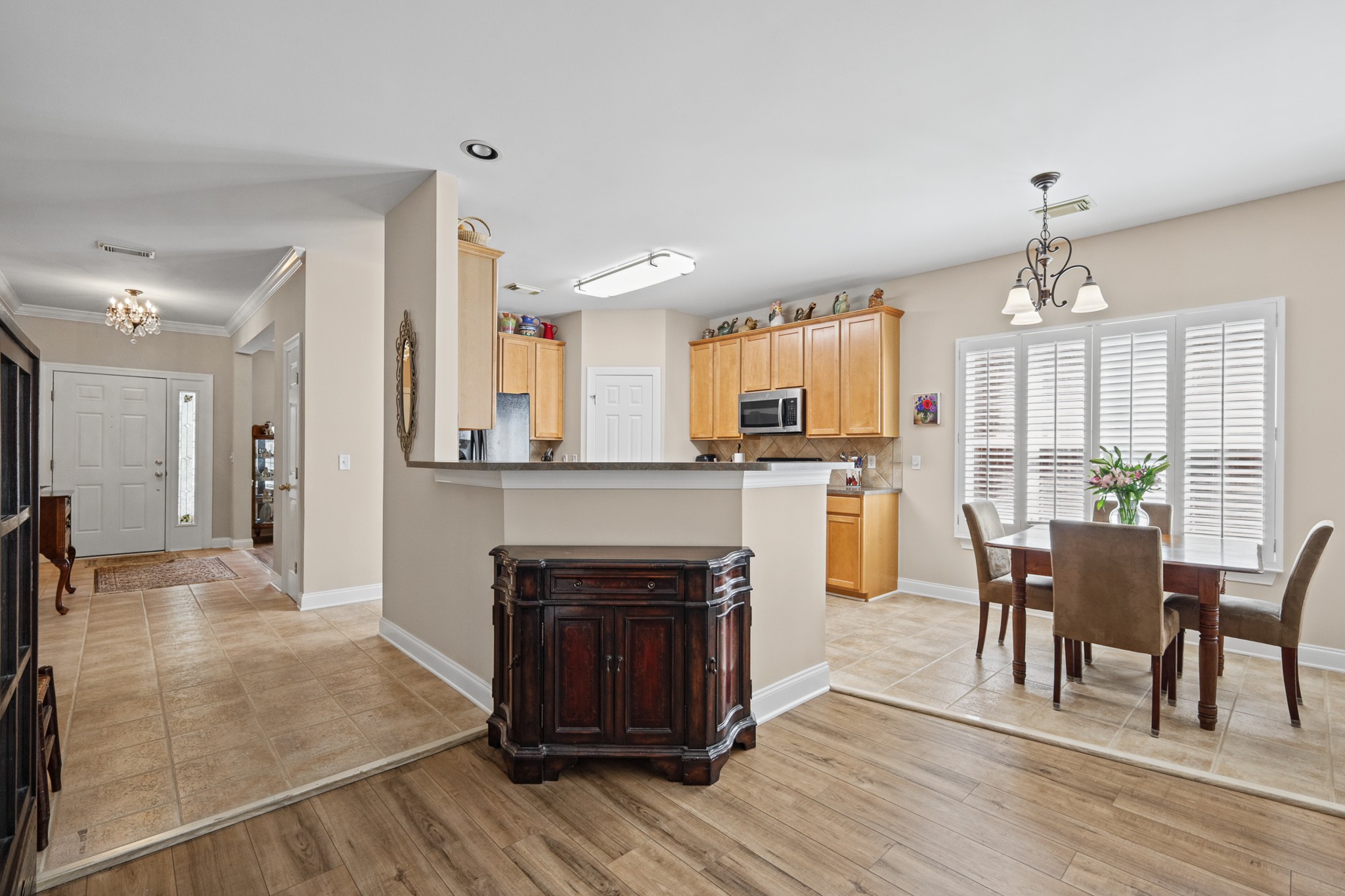 Kitchen and dining area with honey wood cabinets, breakfast bar, and a table by shuttered windows.
