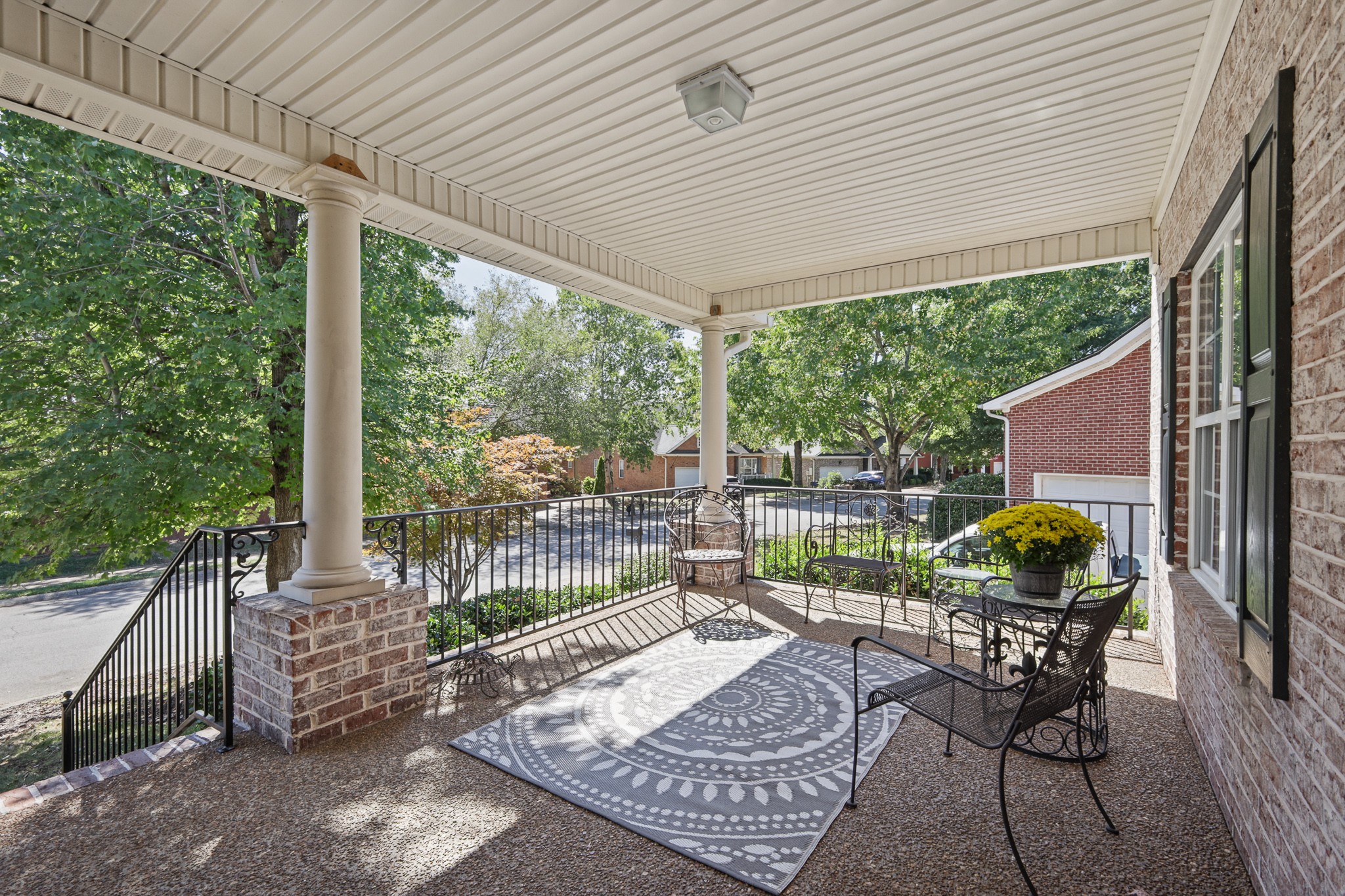 Covered brick front porch with white columns, black railings, outdoor seating, and a patterned rug.