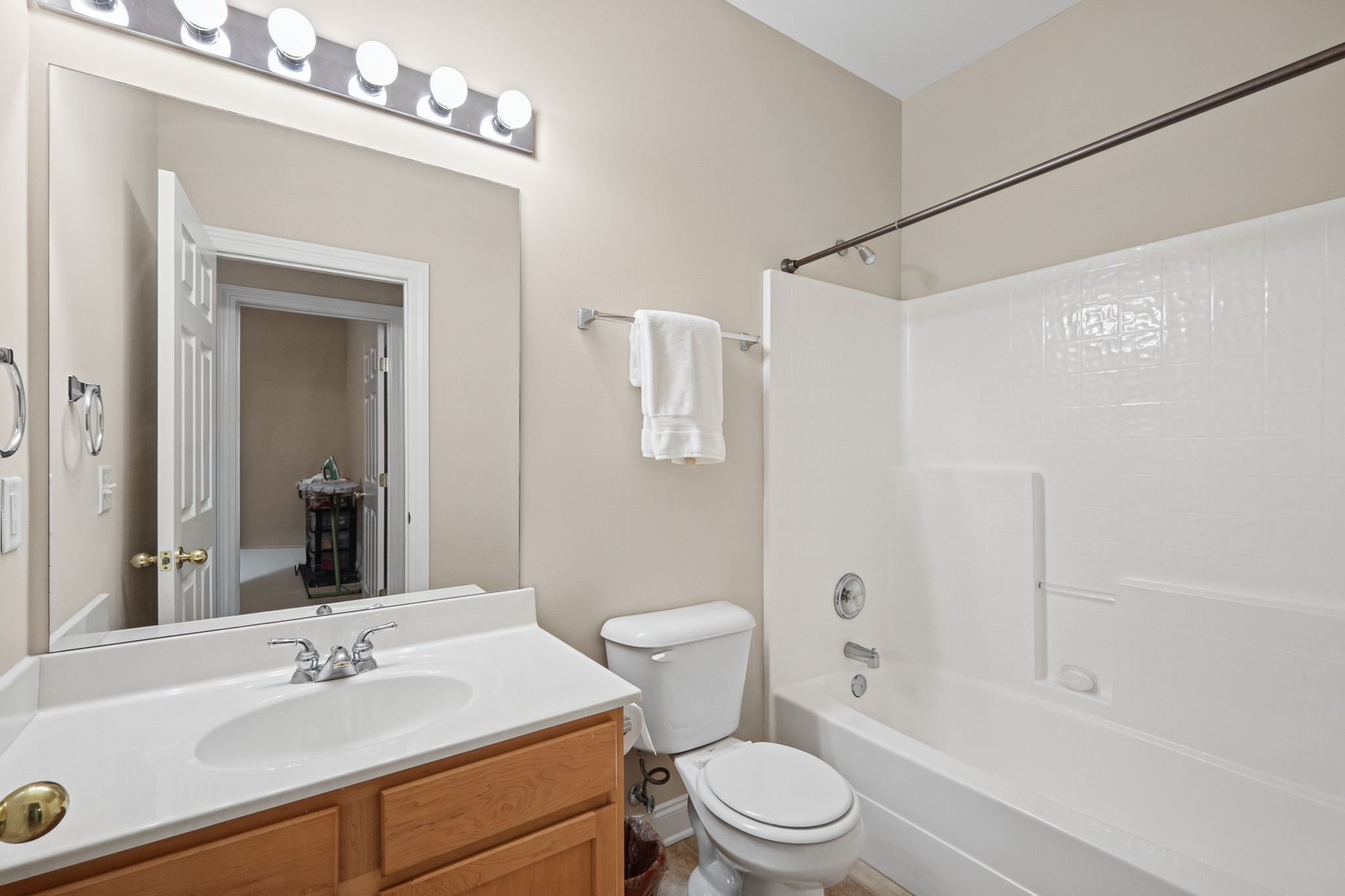 Bathroom with a white tub and shower, large mirror, and wood-cabinet vanity.