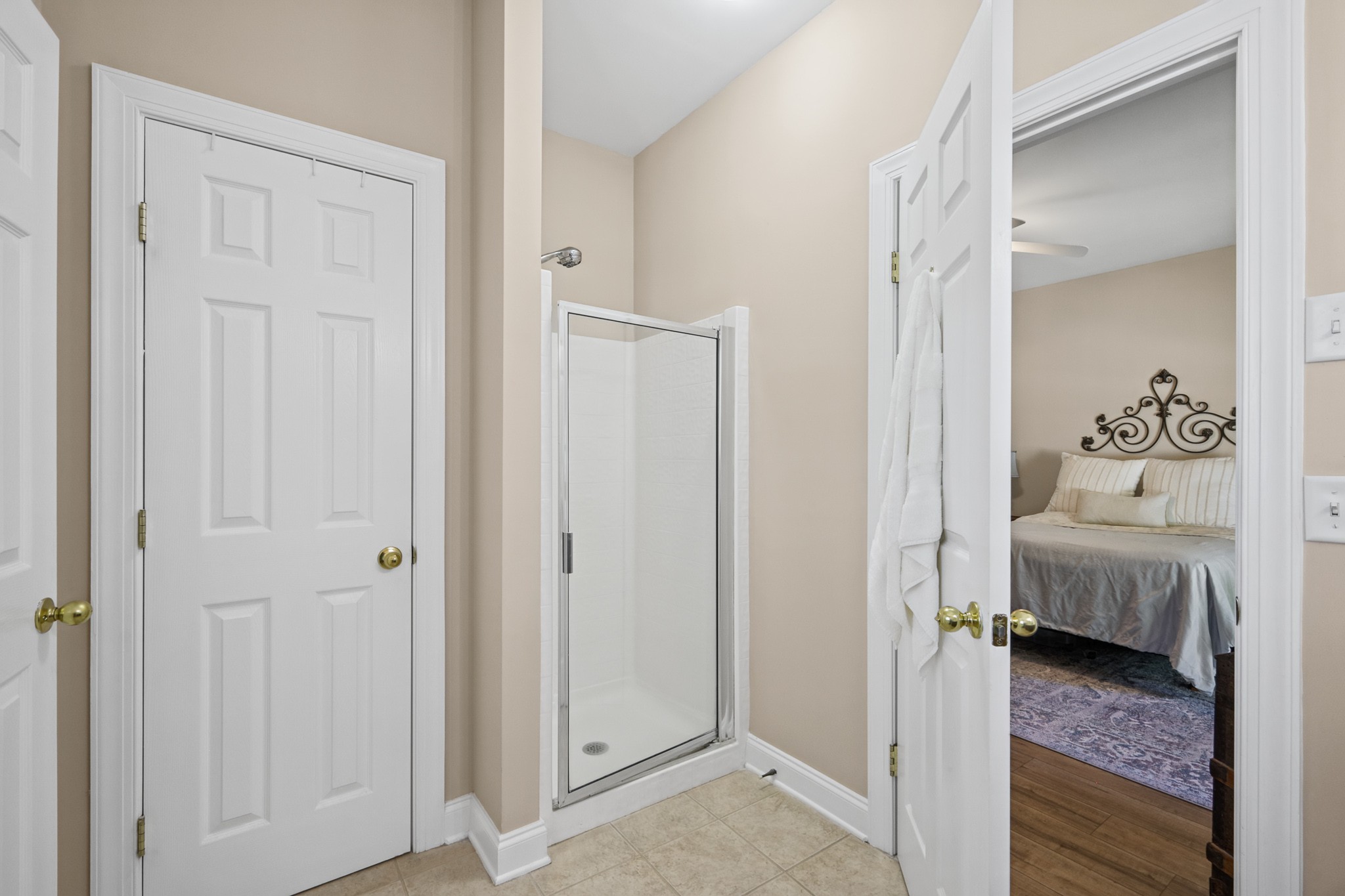 Bathroom with glass shower and tiled floor, viewed through an open doorway to a bedroom.
