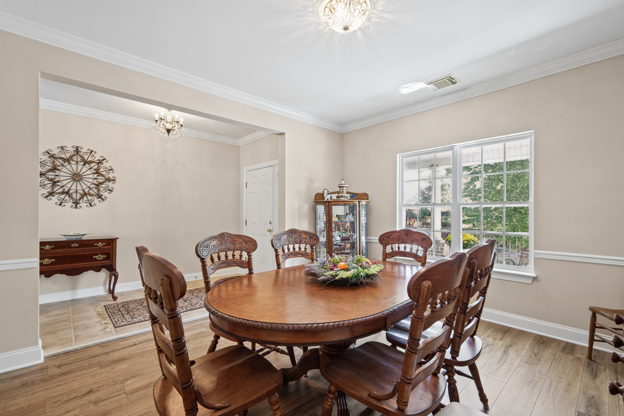 Dining room with a carved wooden table, matching chairs, chandelier, and large garden-facing window.