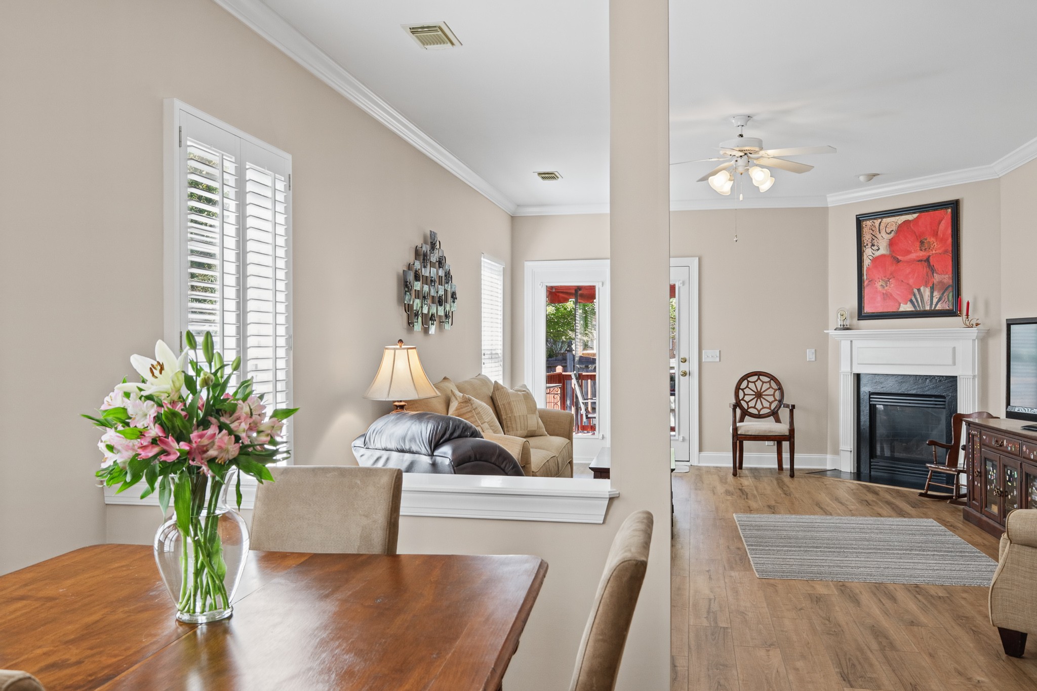 Living room and dining area with a fireplace, plantation shutters, and flowers on the table.