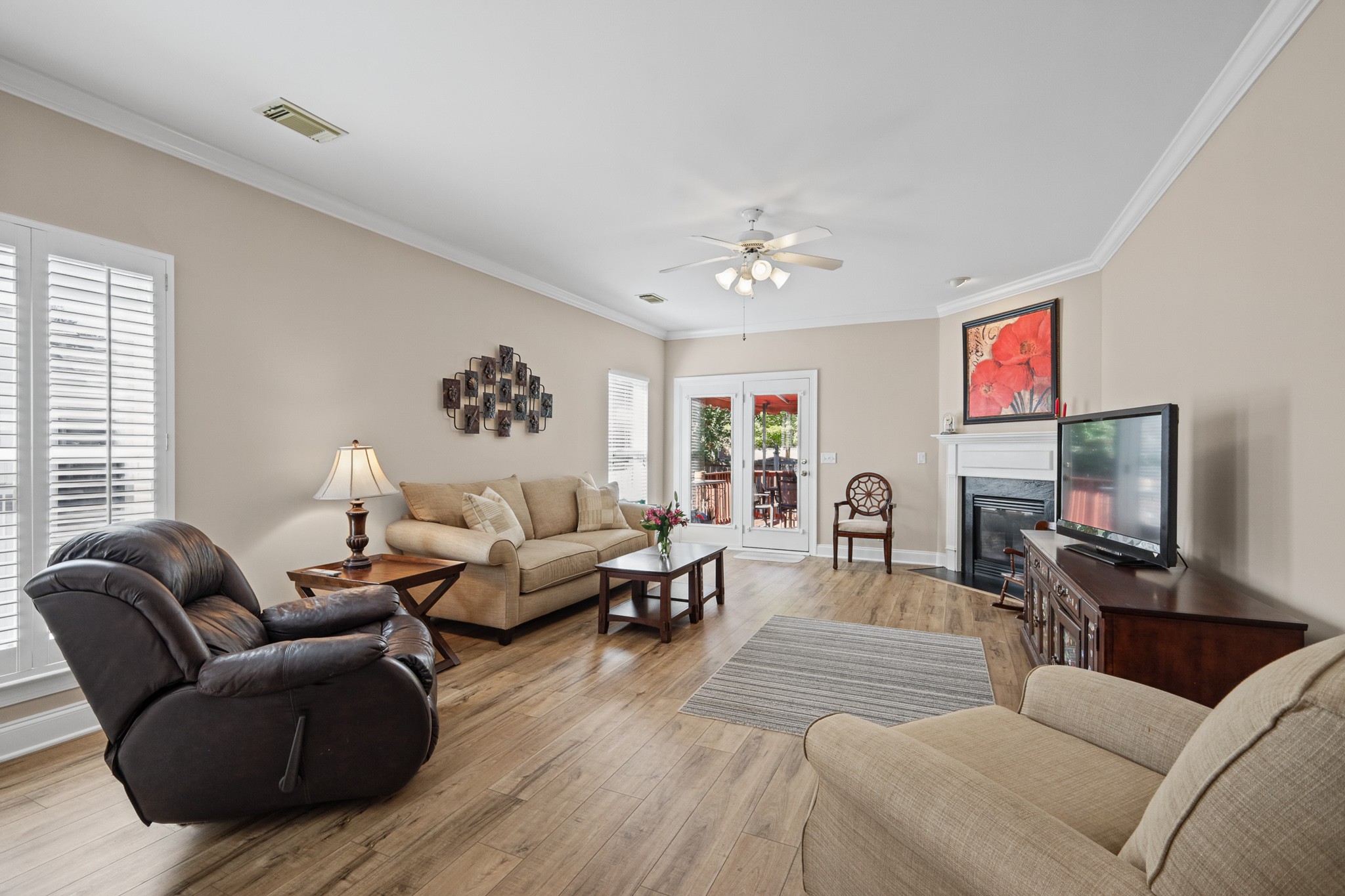 Living room with beige sofas, a dark leather recliner, wood floors, fireplace, and patio doors.