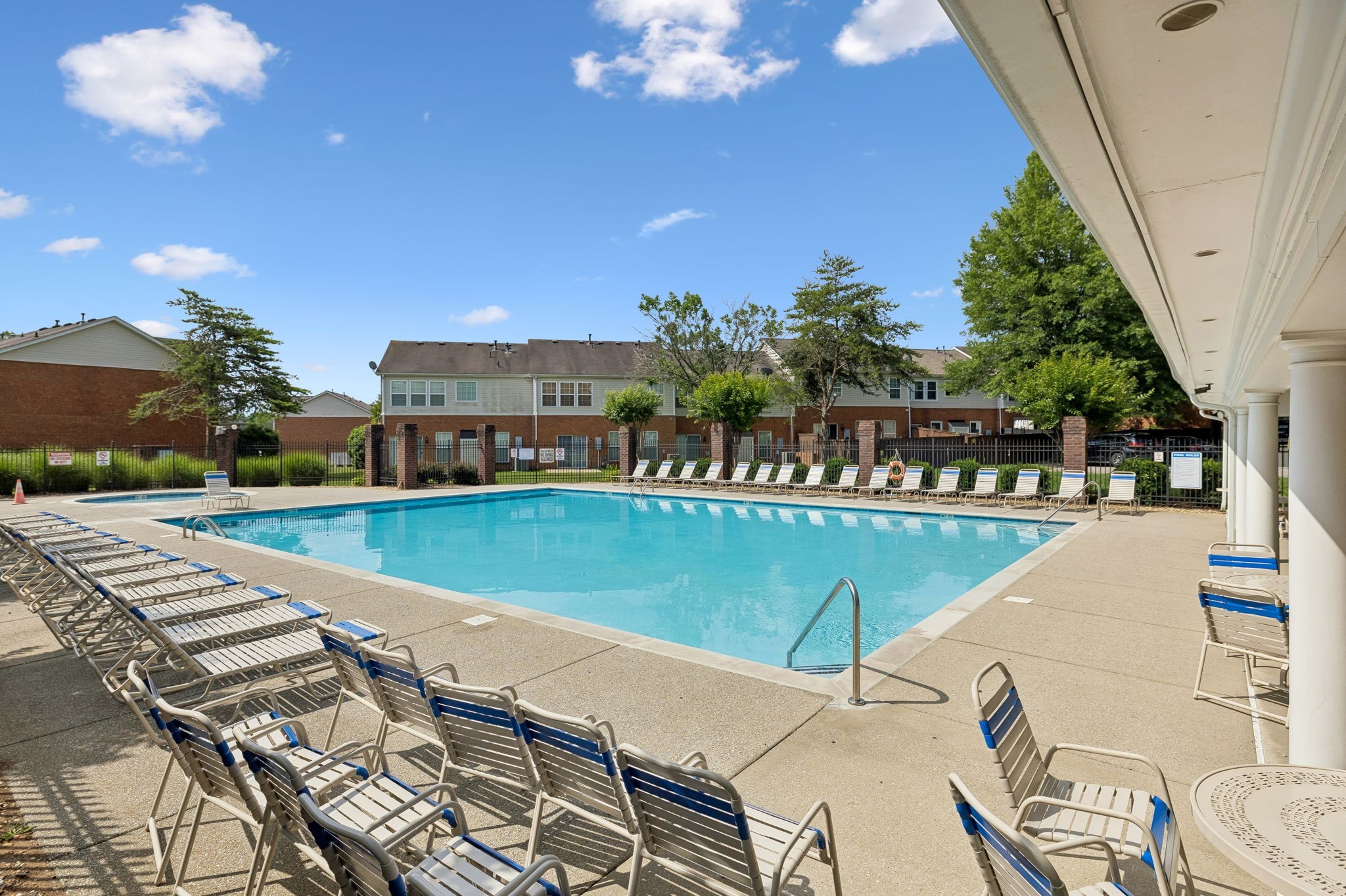 Community pool with blue water, rows of lounge chairs, and residences beyond the fence.
