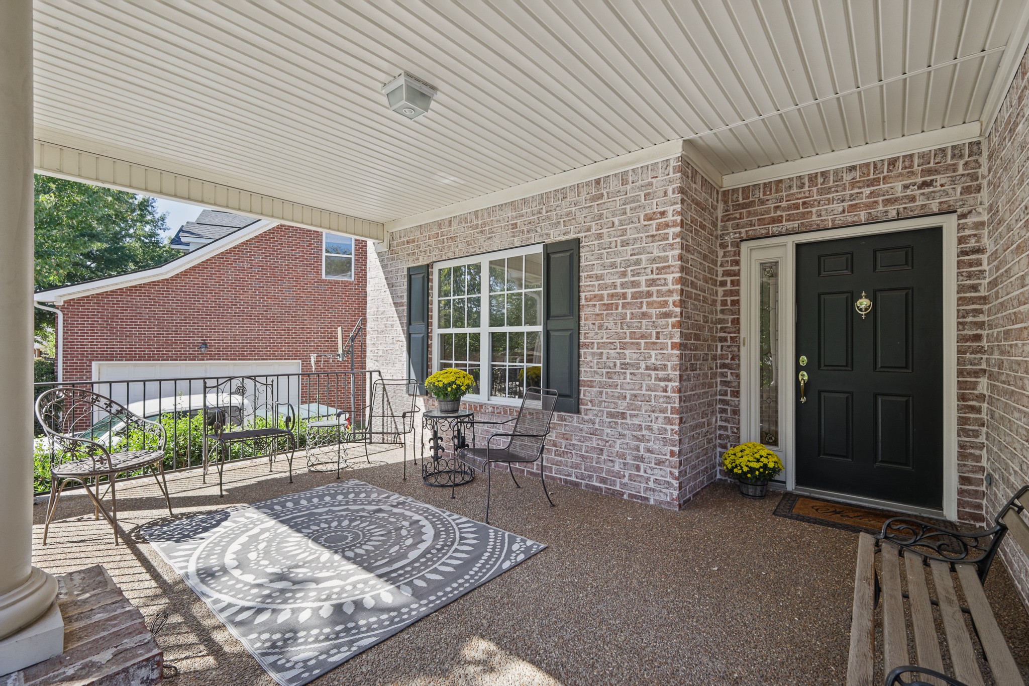 Covered brick front porch with black entry door, metal patio seating, and patterned rug.