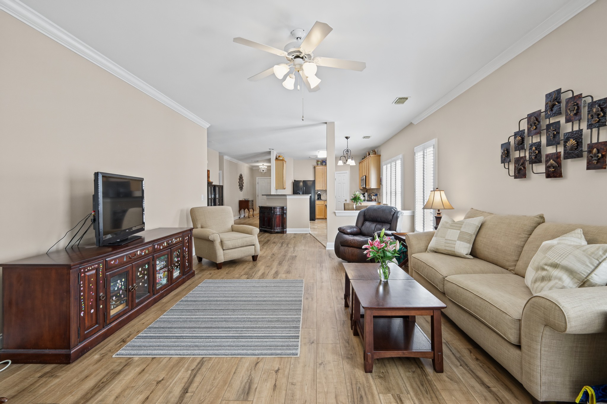 Furnished living room with a beige sofa, wood-look flooring, and an open view into the kitchen.