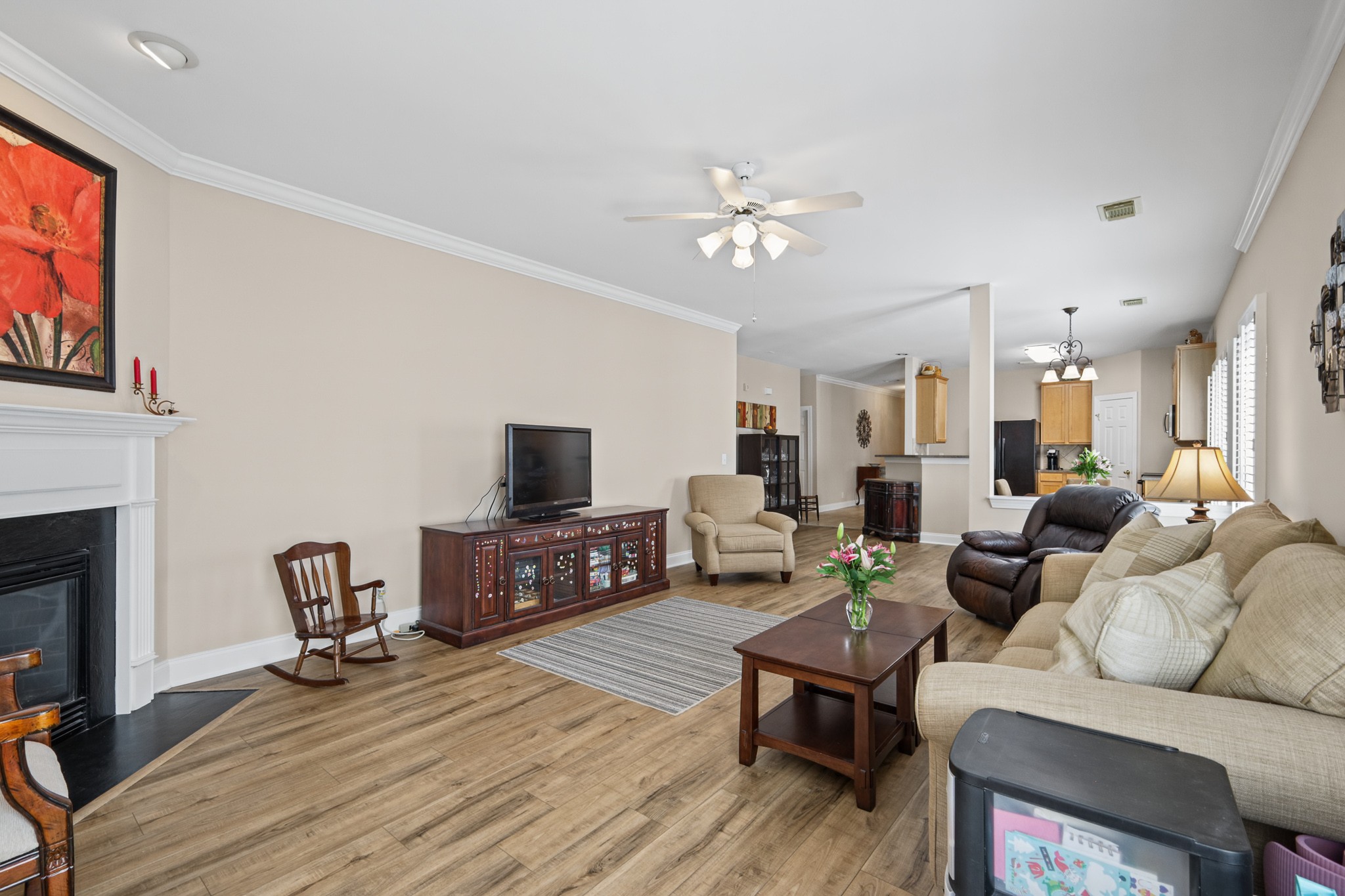 Living room with a white fireplace, wood-look floors, and an open kitchen beyond the seating area.