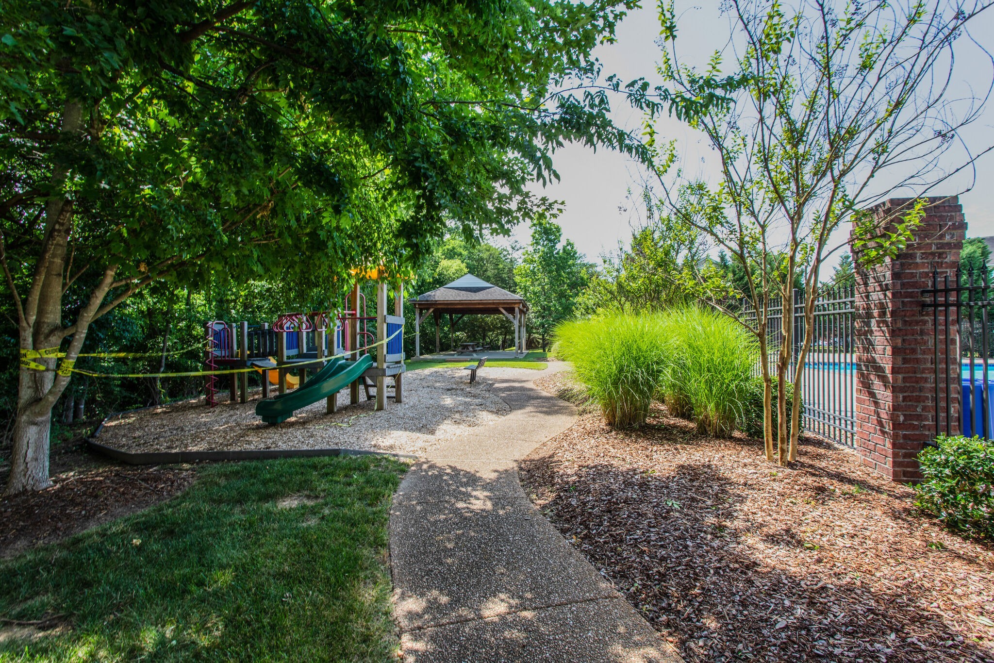 Playground with a green slide beside a fenced swimming pool and paved path.