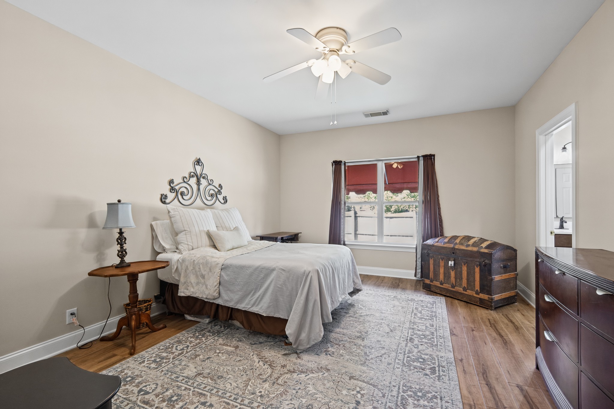 Bedroom with a white bed, patterned rug, ceiling fan, and antique wooden chest.