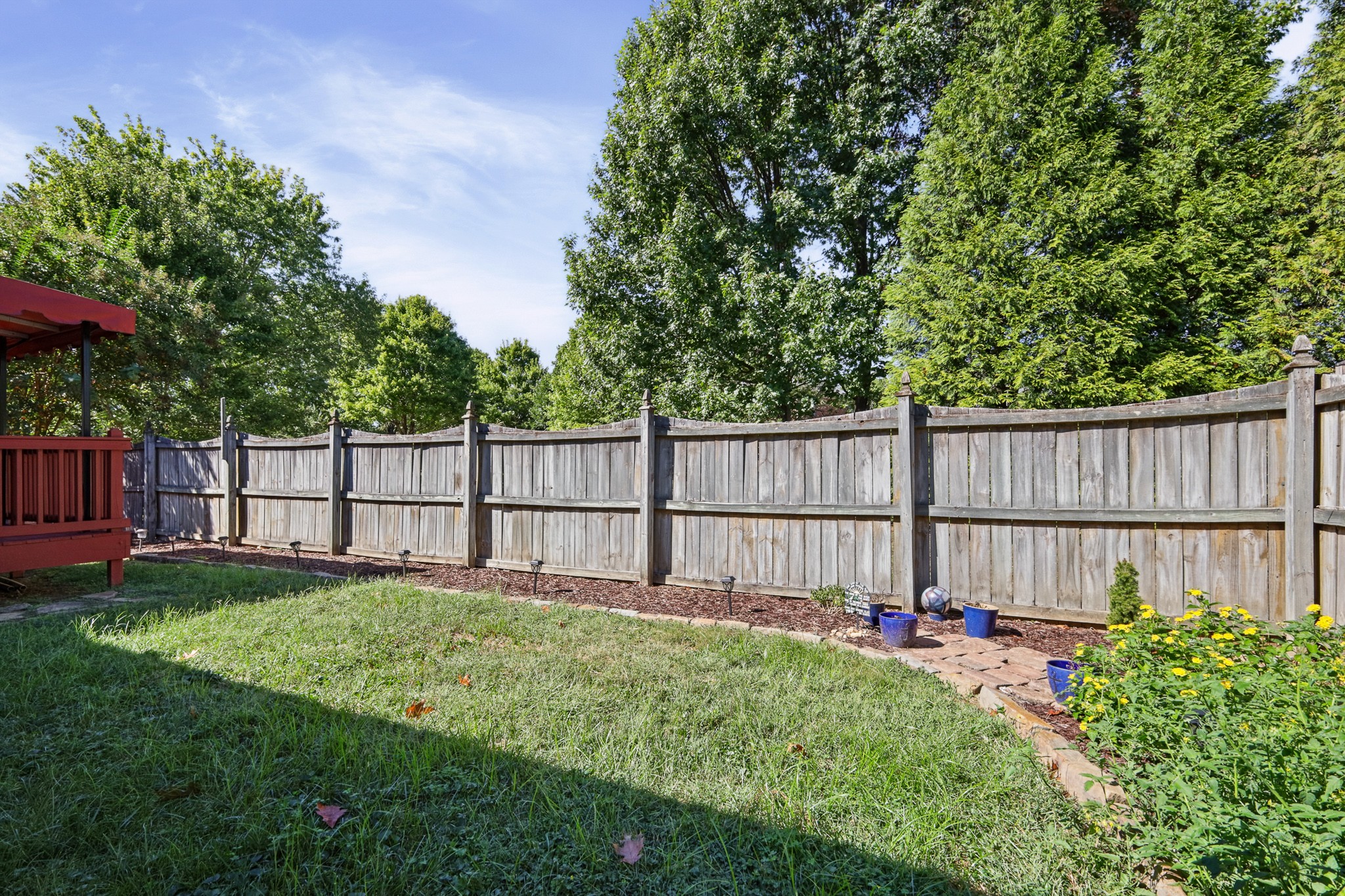 Fenced backyard with a wide lawn, red deck, and planted flower beds along the fence.