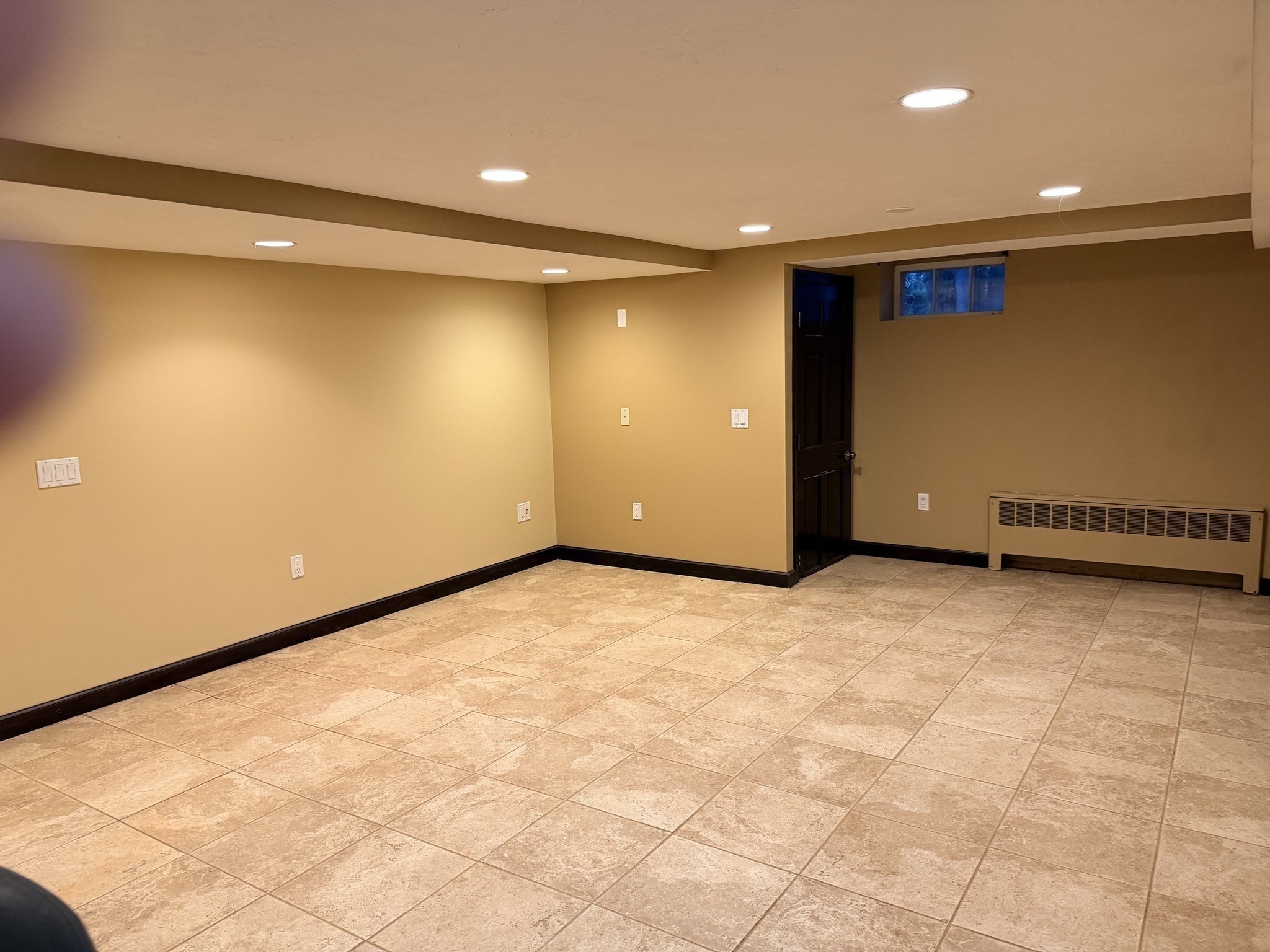 Empty finished basement with a tiled floor, recessed lights, and a small high window.