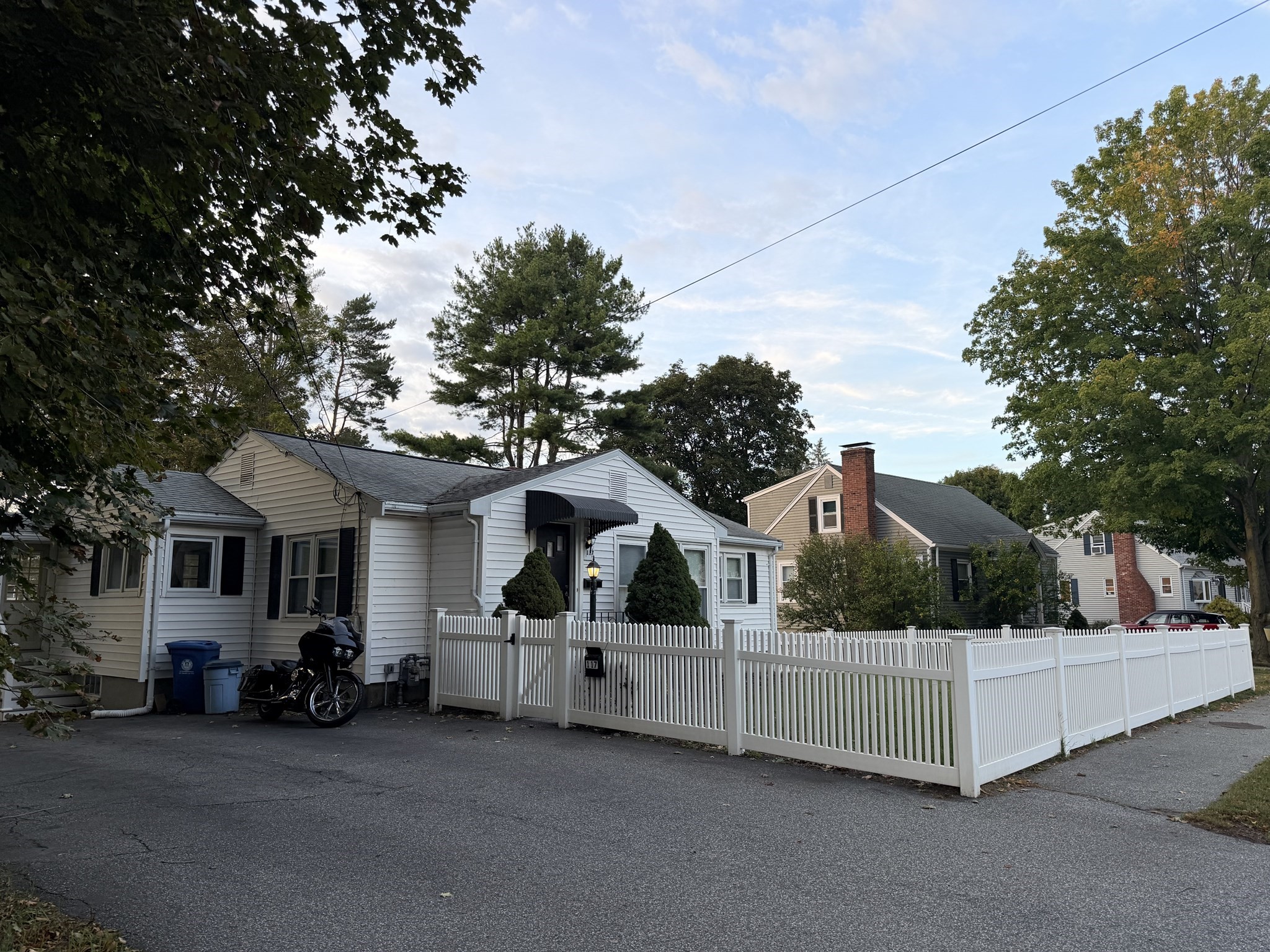 White single-story home with a black entry awning behind a white picket fence.