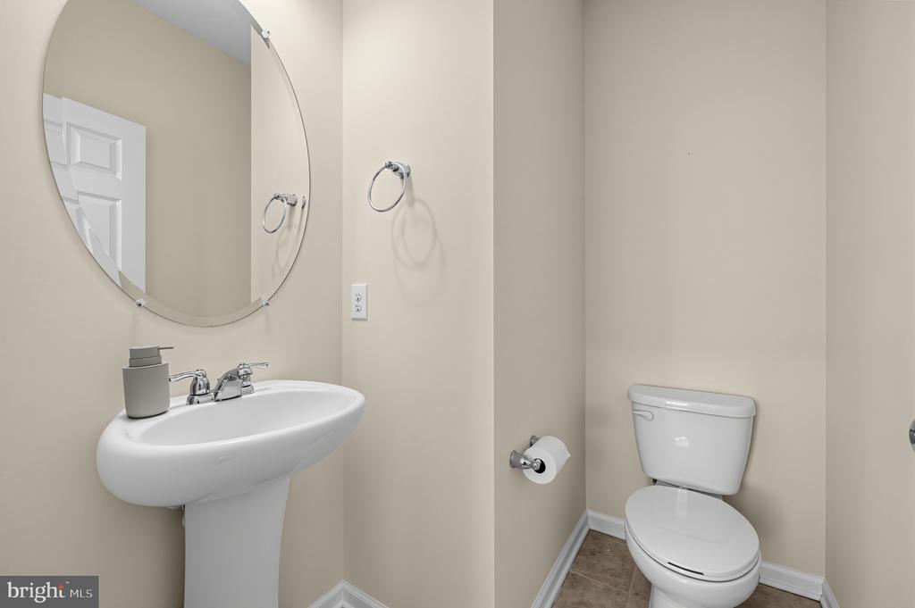 Half bathroom with a white pedestal sink, toilet, and large oval mirror.