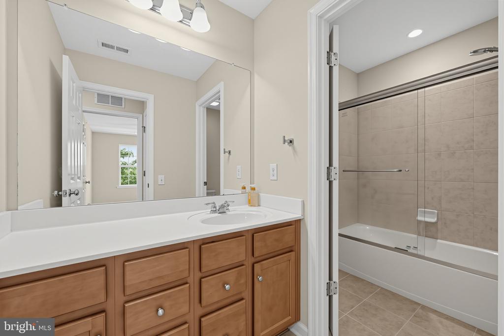 Bathroom with a wood vanity and a tiled tub-shower behind sliding glass doors.