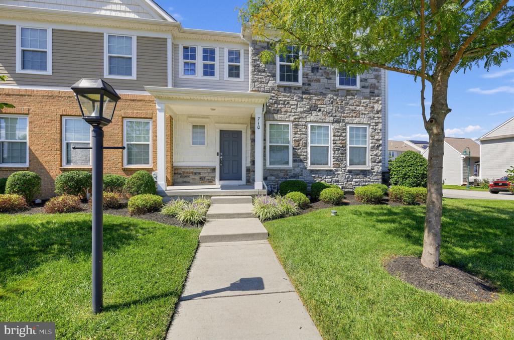 Townhouse entrance with gray stone facade, landscaped lawn, and a walkway leading to the front door.