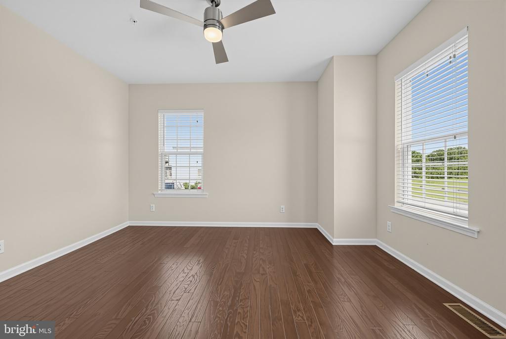 Empty bedroom with hardwood floors, two windows, and a ceiling fan.