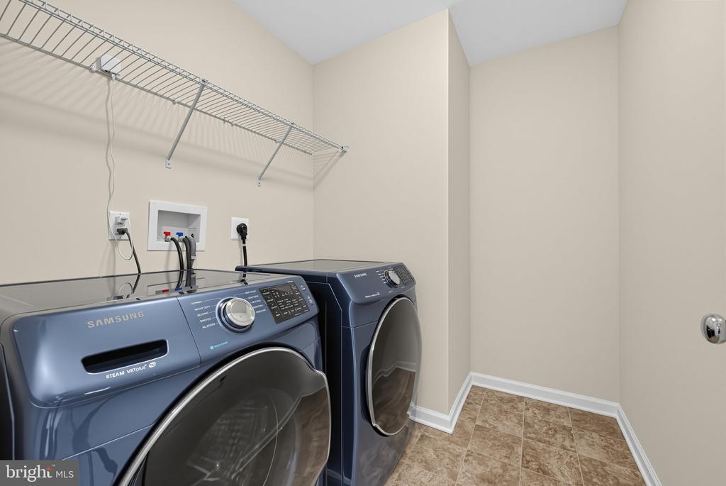 Laundry room with blue front-loading washer and dryer beneath wire shelving.