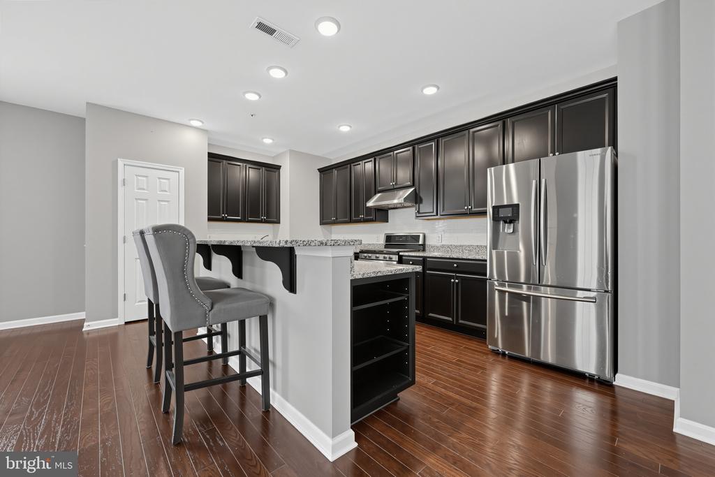 Kitchen with dark cabinets, granite breakfast bar, gray stools, and stainless steel appliances.