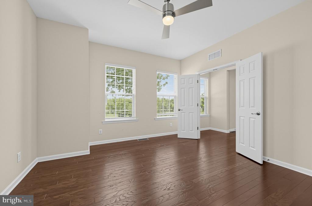 Empty bedroom with dark hardwood floors, a ceiling fan, and windows with white blinds.