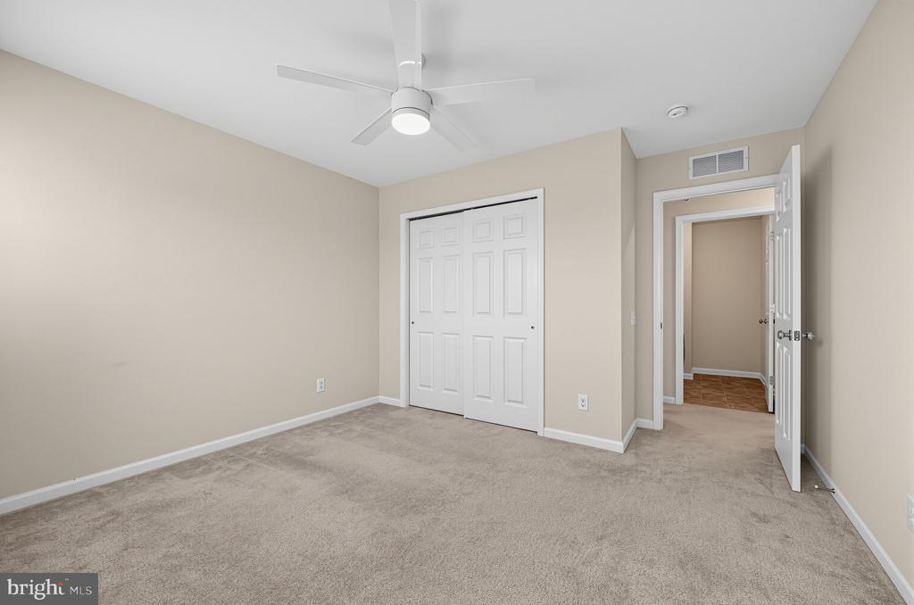 Empty carpeted bedroom with a ceiling fan, double closet doors, and an open doorway.