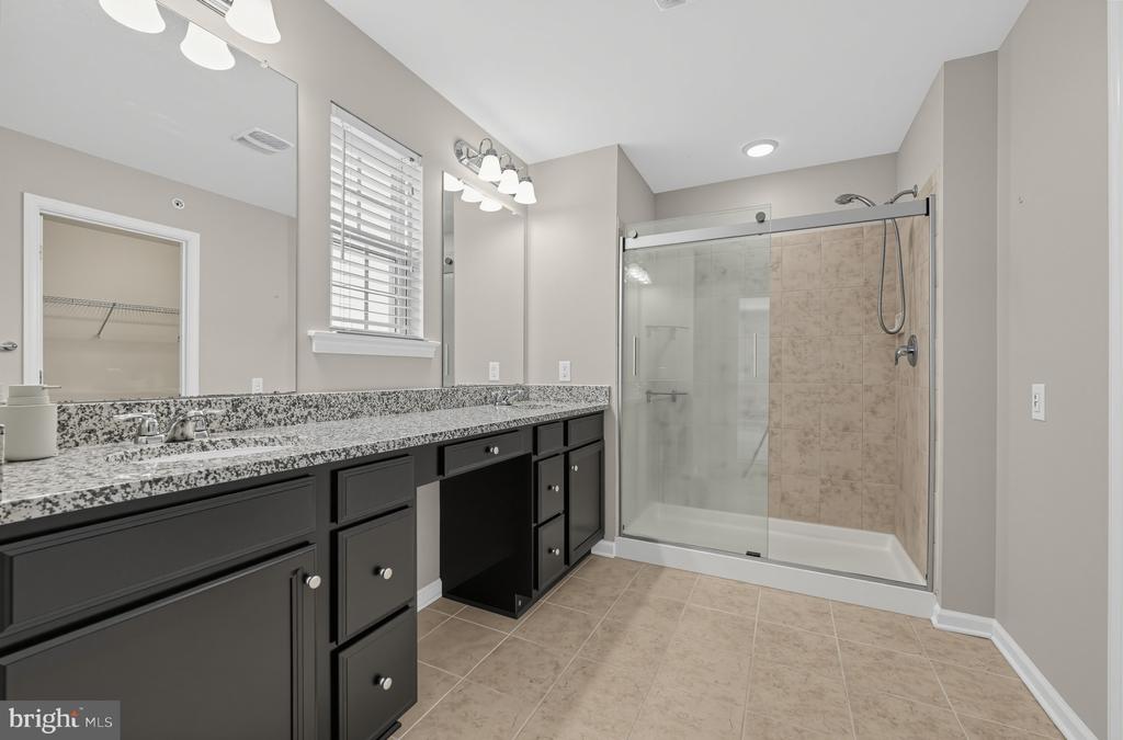 Bathroom with a long dark vanity and granite counter beside a glass-enclosed tiled shower.