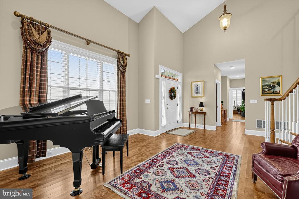Two-story foyer with a grand piano, large window, patterned rug, and staircase.