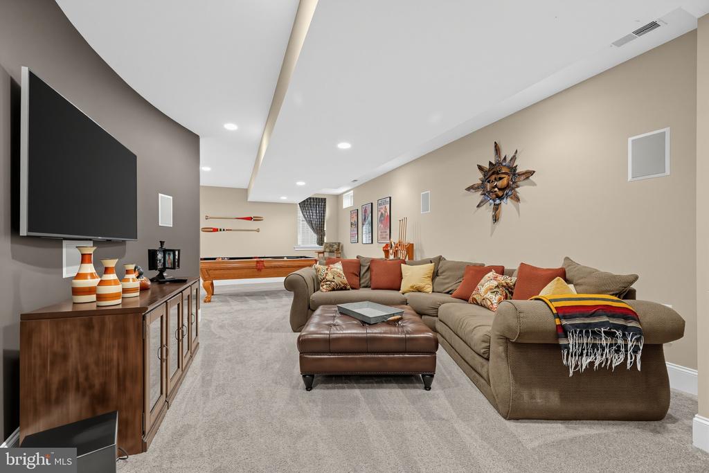 Furnished recreation room with a sectional sofa, wall-mounted TV, and shuffleboard table.