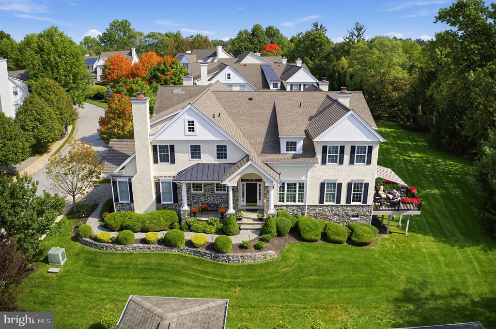 White two-story home with stone foundation, landscaped front garden, and raised deck, viewed from above.