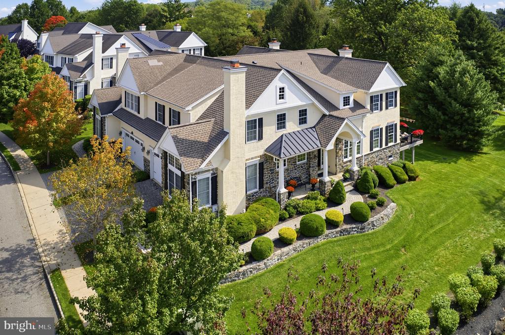 Aerial view of a beige two-story home with stone accents, landscaped gardens, and a broad lawn.