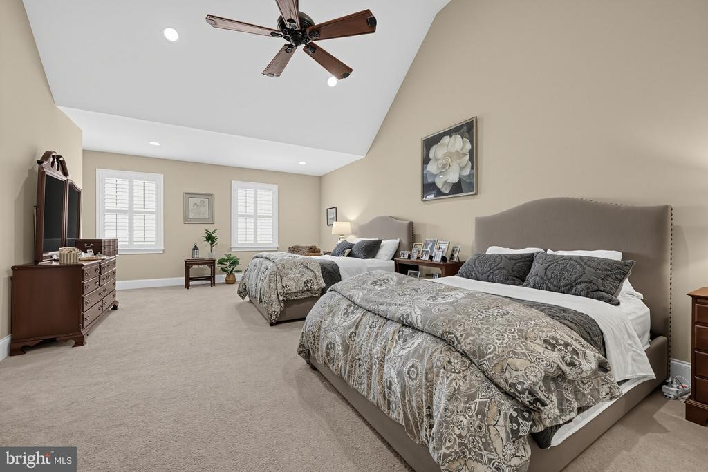 Spacious bedroom with two beds, patterned bedding, and a vaulted ceiling with a ceiling fan.