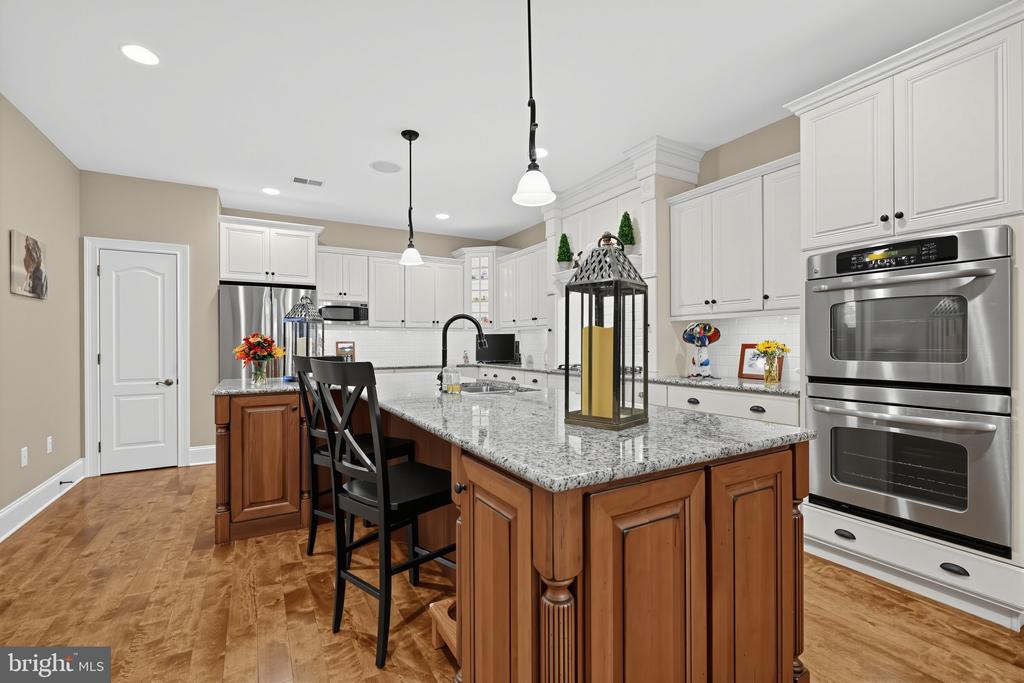 Kitchen with a large granite island, white cabinets, stainless steel double ovens, and hardwood floors.