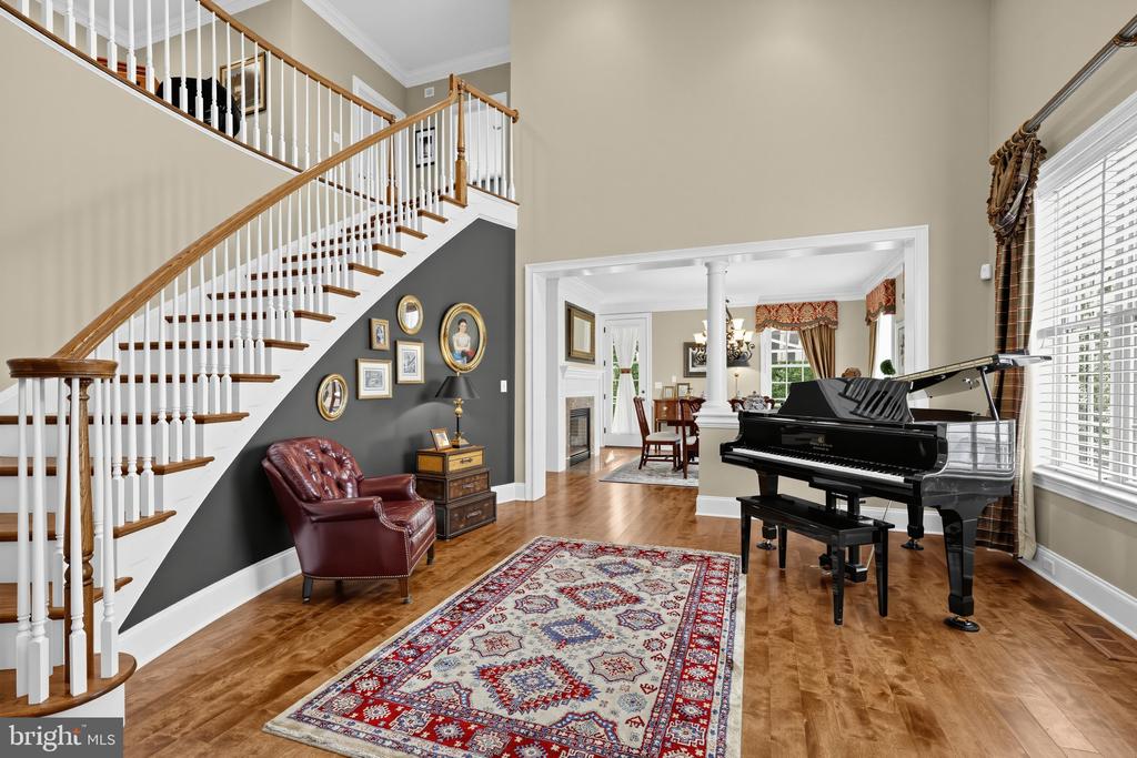 Living room with a grand staircase, patterned rug, and black grand piano.