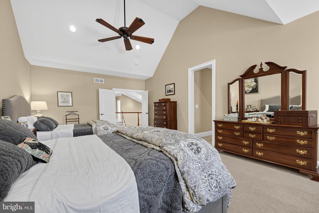 Furnished bedroom with gray patterned bedding, a mirrored wood dresser, and a vaulted ceiling.