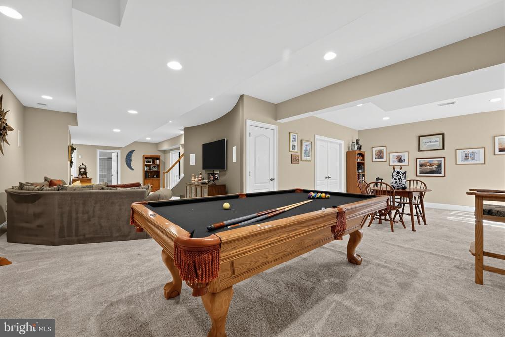 Furnished recreation room with a wooden pool table, sofa seating, and a small dining area.