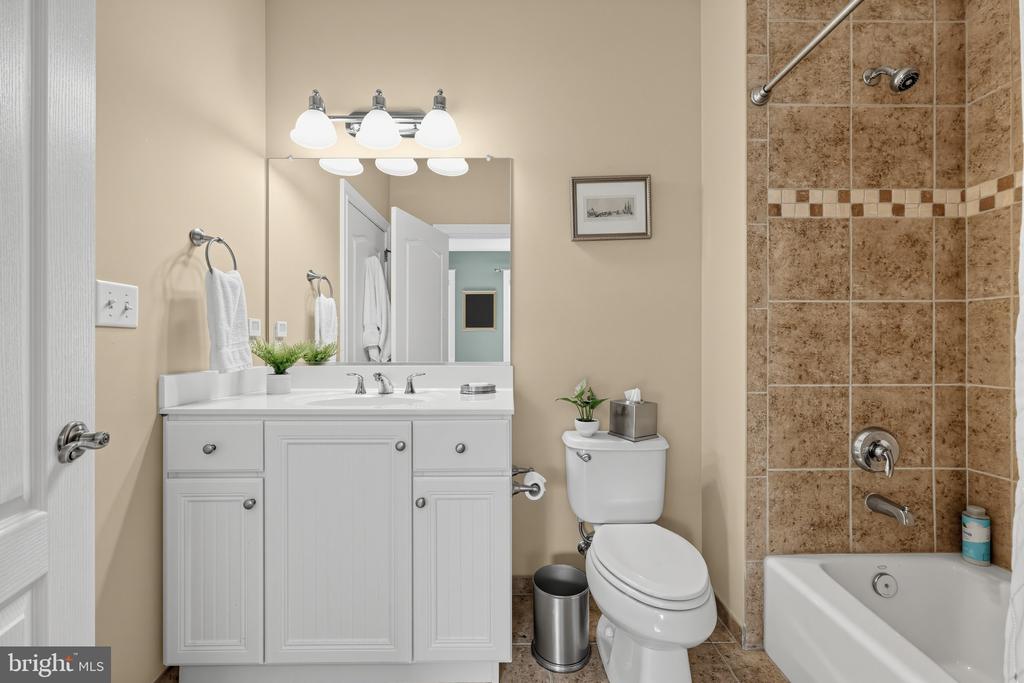Bathroom with a white double-sink vanity and a bathtub with brown tiled surround.
