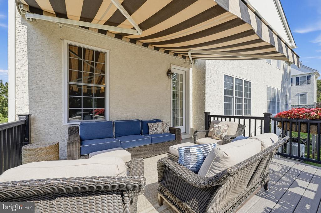 Furnished house deck with wicker seating, blue cushions, and a striped awning.