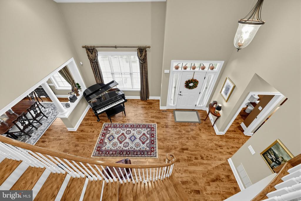 Two-story foyer with a curved staircase, hardwood floors, and a black grand piano.