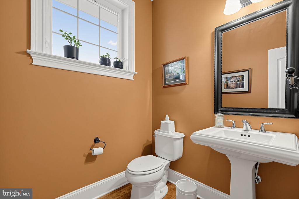 Bathroom with ochre walls, a white pedestal sink, large mirror, and high window with potted plants.